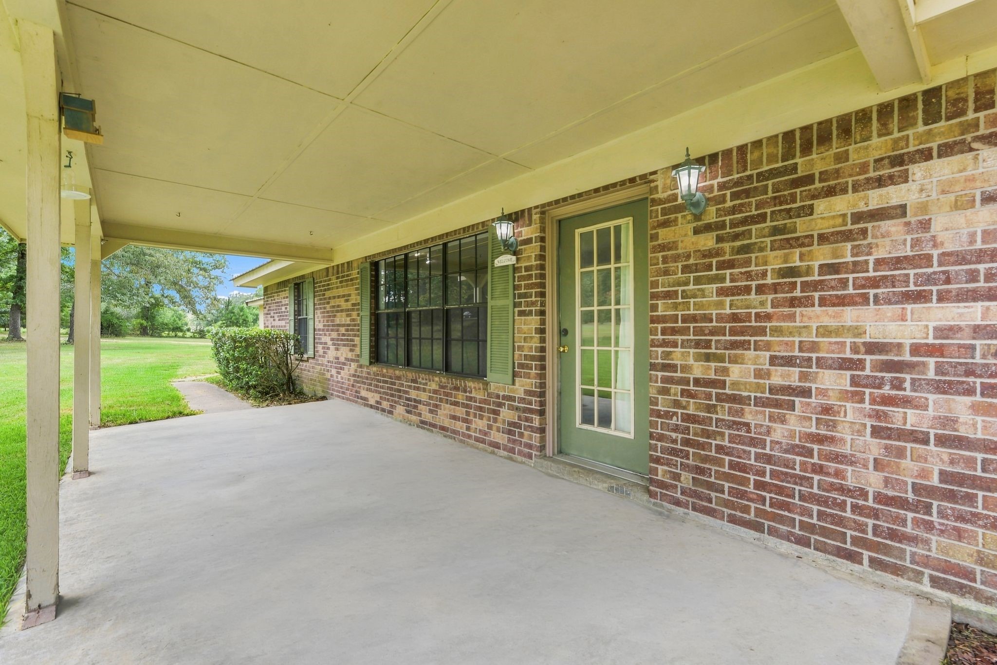 151 Parker Road New Waverly, TX 77358 - Photo 27 of 36 Charming covered patio with brick exterior and elegant lighting, offering a welcoming entrance and perfect spot to enjoy the serene, green surroundings.