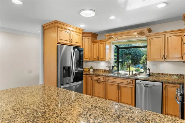 a kitchen with stainless steel appliances granite countertop a refrigerator a sink dishwasher and wooden cabinets