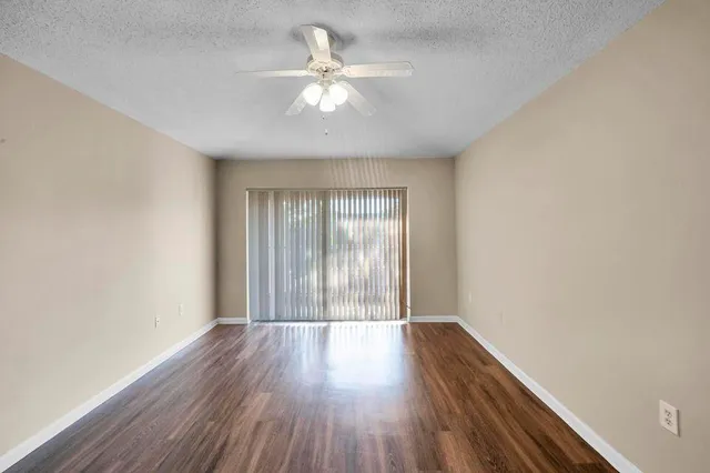 an empty room with wooden floor fan and windows