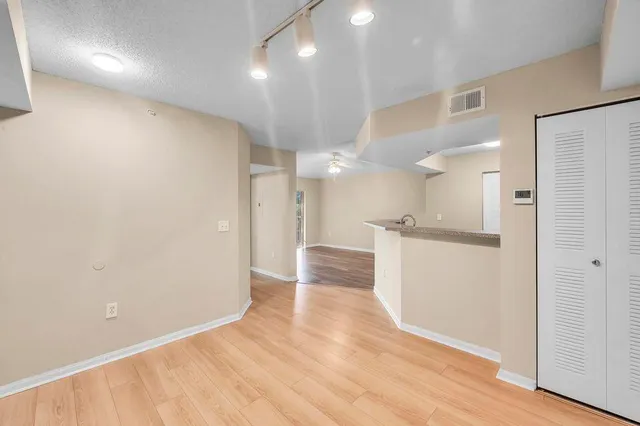 a view of an empty room and kitchen with hardwood floor