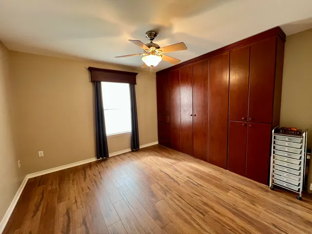 a view of an empty room with wooden floor and a ceiling fan