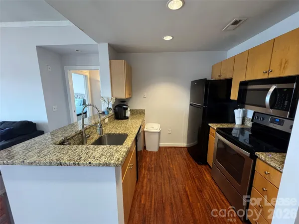 a kitchen with granite countertop kitchen island stainless steel appliances a stove a sink a refrigerator wooden floor and cabinets