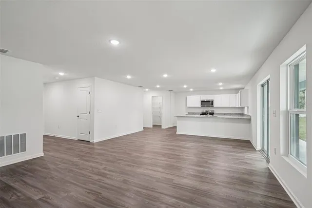 a view of kitchen with kitchen island granite countertop a refrigerator oven a sink and white cabinets with wooden floor