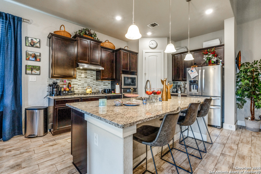 1712 Delafield Road San Antonio, TX 78253 - Photo 7 of 25 a kitchen with stainless steel appliances kitchen island granite countertop a table chairs in it and wooden floors