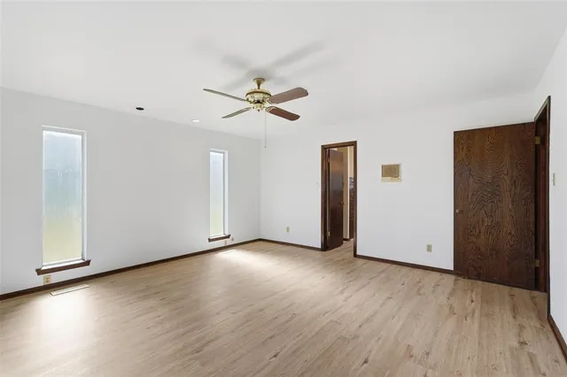a view of an empty room with wooden floor and a ceiling fan