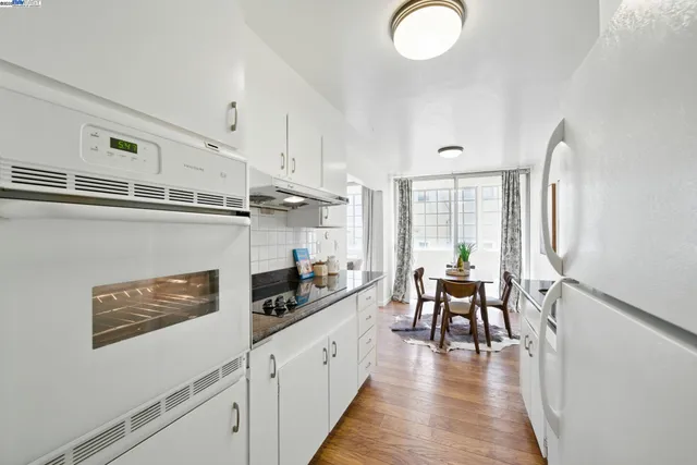 a kitchen with stainless steel appliances granite countertop a refrigerator a stove and white cabinets with wooden floor