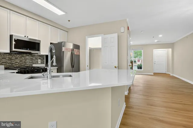 a view of a kitchen with kitchen island a sink wooden floor and stainless steel appliances
