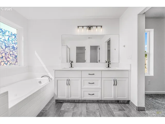 a spacious bathroom with a double vanity sink a mirror a bathtub and next to a window