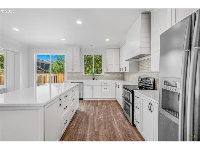 a kitchen with granite countertop a refrigerator oven a sink dishwasher and white cabinets with wooden floor