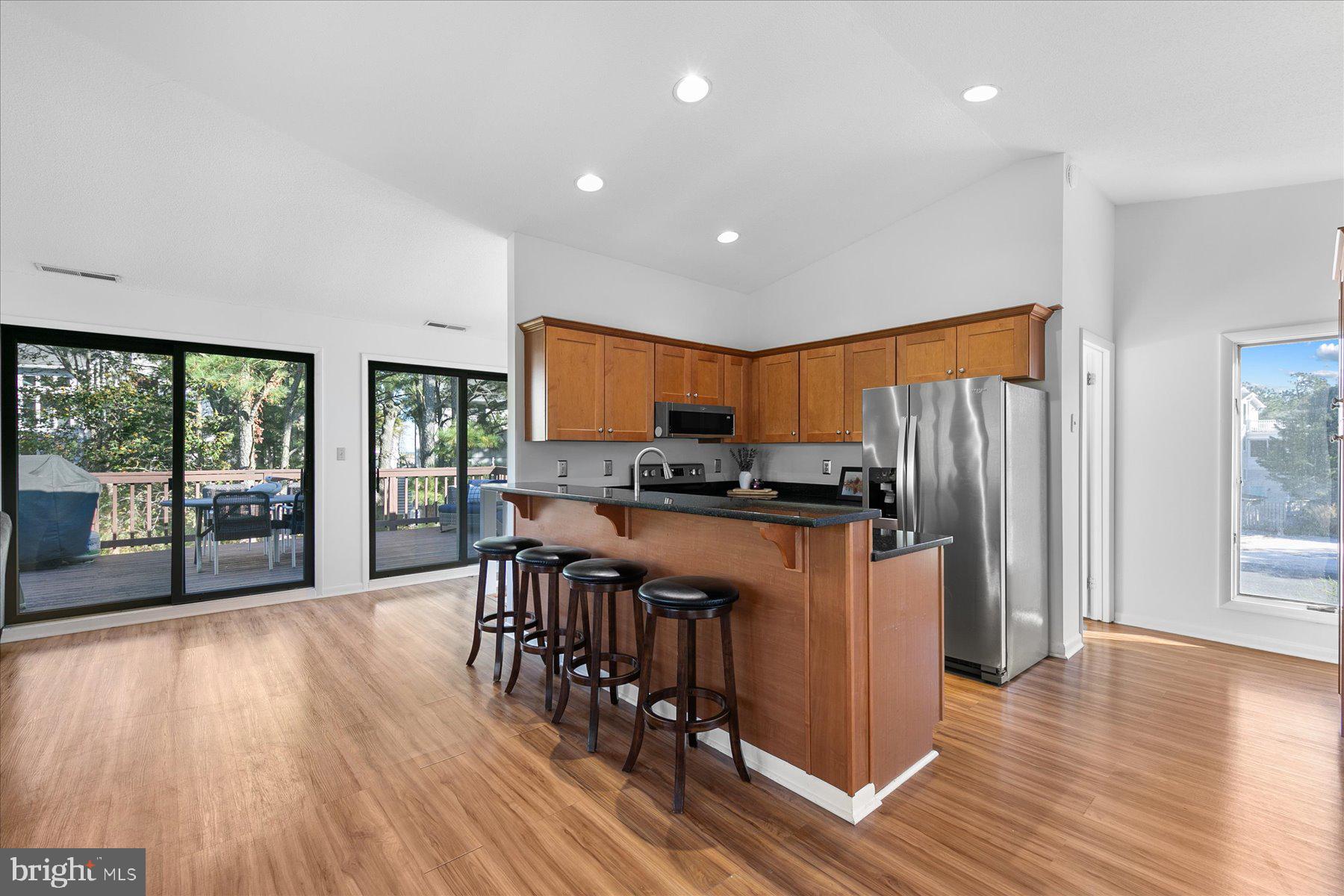 39692 Kittiwake Road Bethany Beach, DE 19930 - Photo 9 of 32 a kitchen with stainless steel appliances granite countertop a refrigerator a sink dishwasher a stove and a dining table with wooden floor