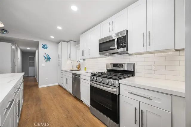 a kitchen with stainless steel appliances granite countertop white cabinets a sink a stove a microwave and a refrigerator