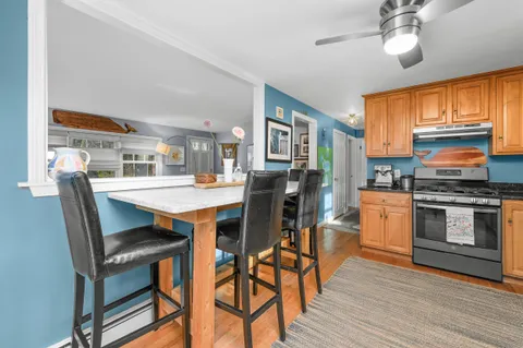 a kitchen with stainless steel appliances granite countertop a stove a refrigerator a kitchen island a dining table and chairs with wooden floor