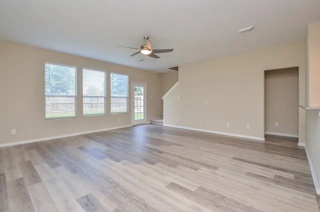 an empty room with wooden floor chandelier fan and windows
