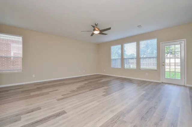 an empty room with wooden floor ceiling fan and windows
