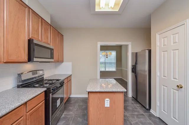 a kitchen with stainless steel appliances granite countertop a stove top oven a sink dishwasher and a refrigerator with wooden cabinets