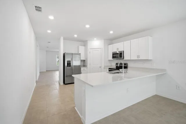 a large white kitchen with a sink a refrigerator and a stove top oven with wooden floor