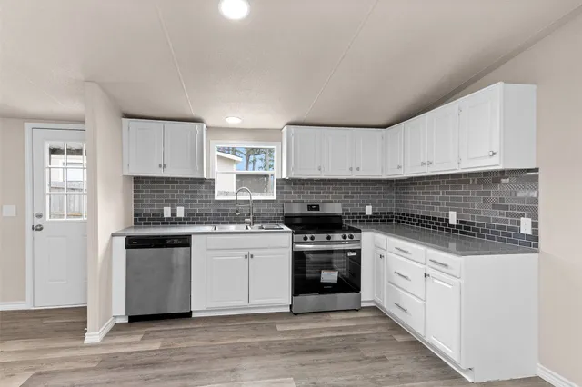 a large kitchen with stainless steel appliances granite countertop a stove a sink and white cabinets