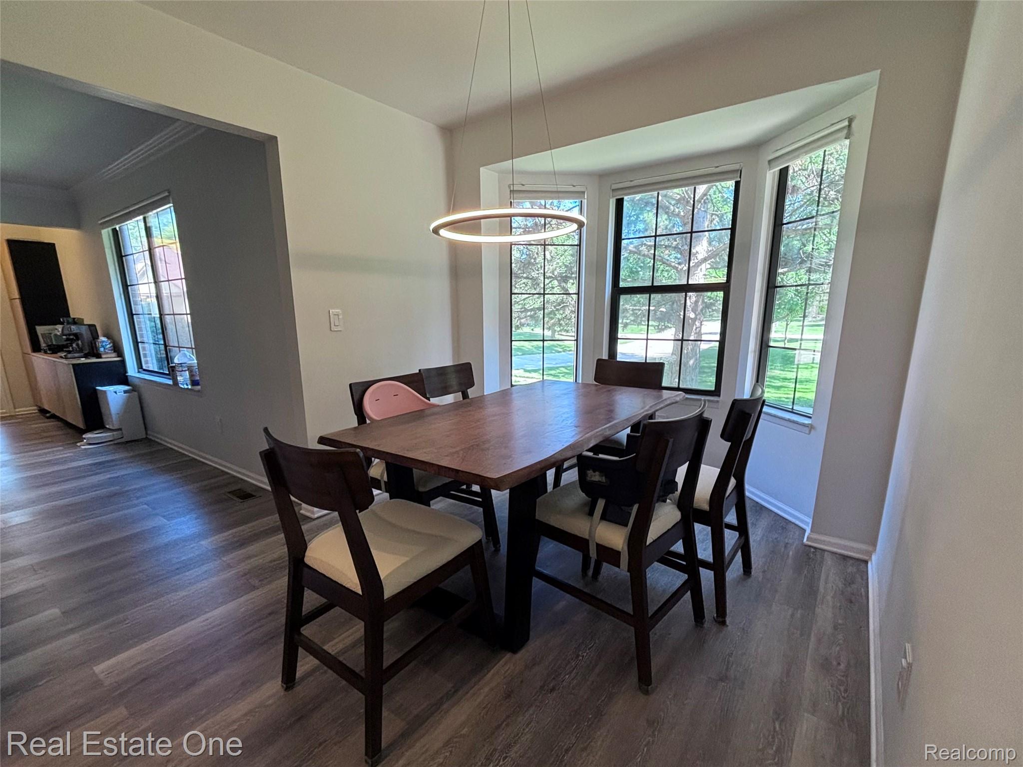 66 Meadow Wood Drive Rochester, MI 48307 - Photo 8 of 20 Dining area with bay windows featuring grid-patterned panes, wood-finish flooring, a modern circular pendant light, and an open archway to an adjacent room