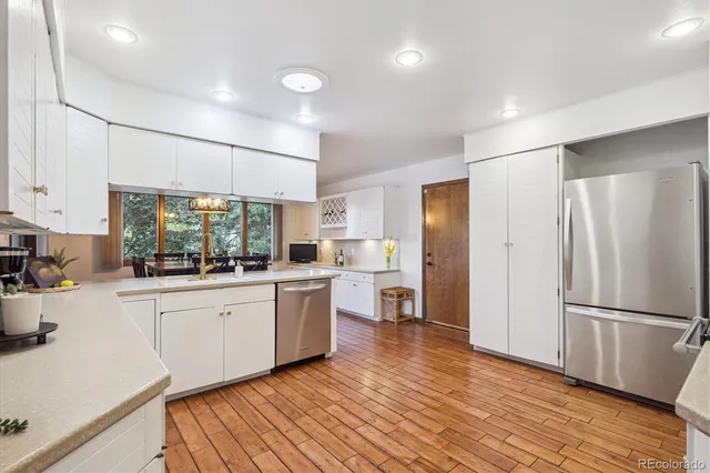 a kitchen with stainless steel appliances granite countertop a refrigerator a sink dishwasher a stove and white countertops with wooden floor