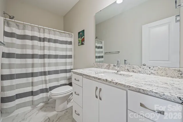 a bathroom with a granite countertop sink a toilet a mirror and shower curtain
