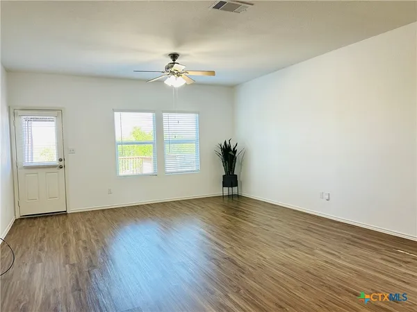 an empty room with wooden floor chandelier fan and windows