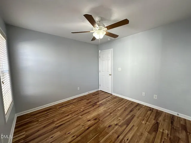 an empty room with wooden floor fan and windows