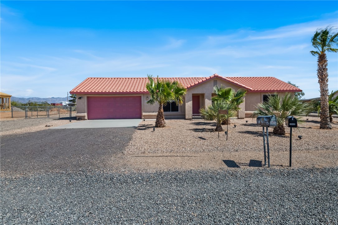 3668 North Neptune Road Golden Valley, AZ 86413 - Photo 2 of 38 The property features a red tiled roof, a pink garage door, and a gravel front yard with palm trees