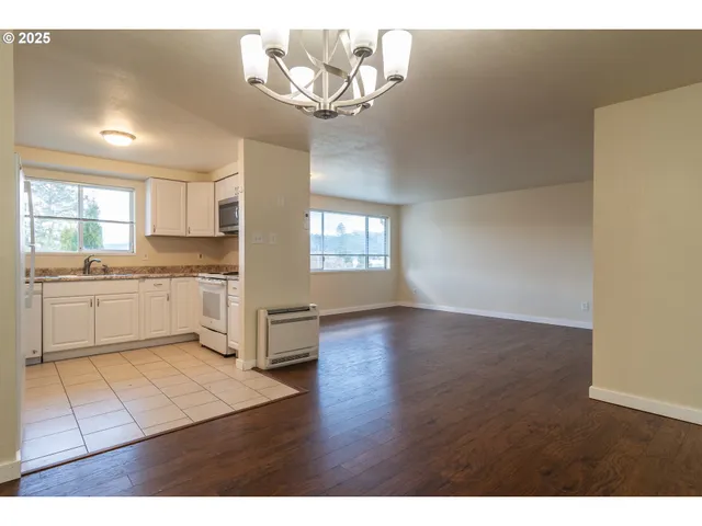 a open kitchen with granite countertop a stove top oven a sink dishwasher and white cabinets with wooden floor