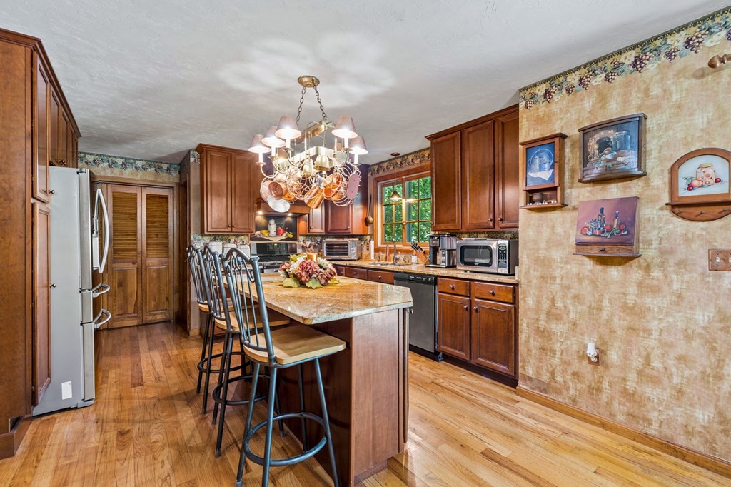 28 Crowell Road Bourne, MA 02562 - Photo 15 of 42 a kitchen with stainless steel appliances kitchen island granite countertop a refrigerator a stove a microwave oven with a dining table and chairs with wooden floor