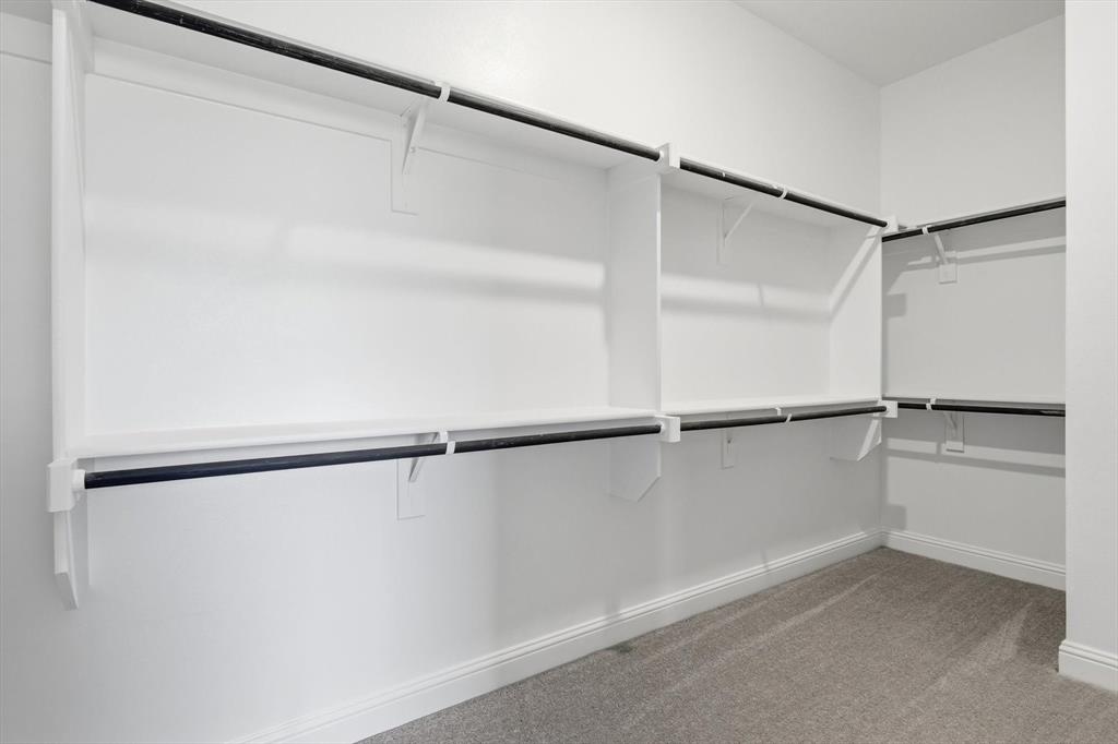 4017 Eagles Bluff Road Midlothian, TX 76065 - Photo 31 of 38 Spacious walk-in closet featuring white built-in shelving, multiple hanging rods, and light gray carpeting