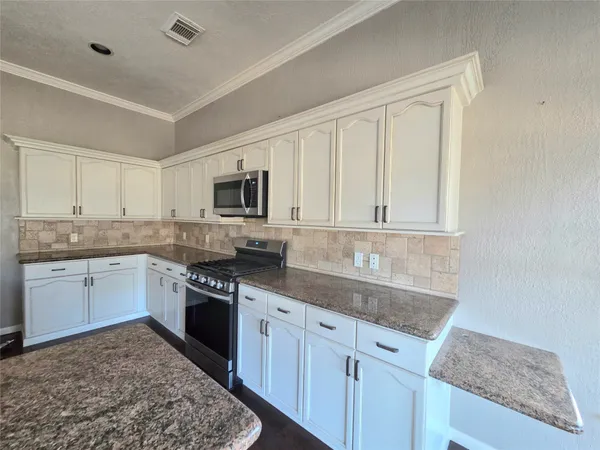 a kitchen with granite countertop a sink stainless steel appliances and white cabinets