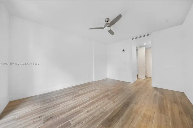 a view of empty room with wooden floor and fan