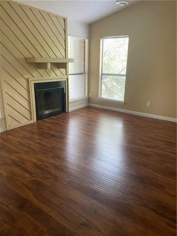 an empty room with wooden floor fireplace and windows