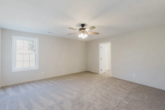 an empty room with chandelier fan and windows