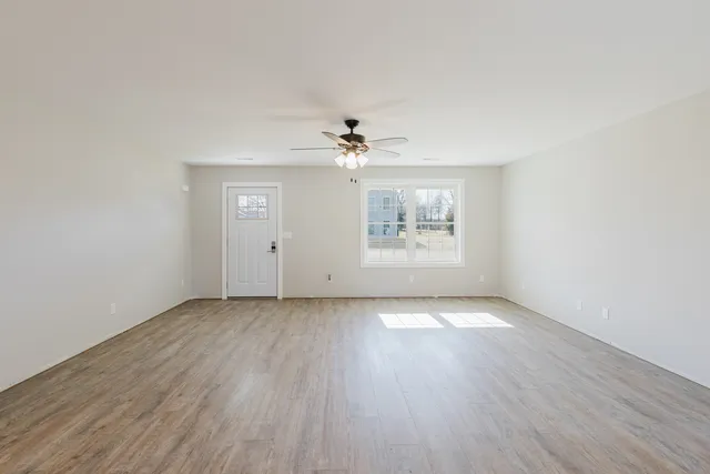 an empty room with wooden floor chandelier fan and windows