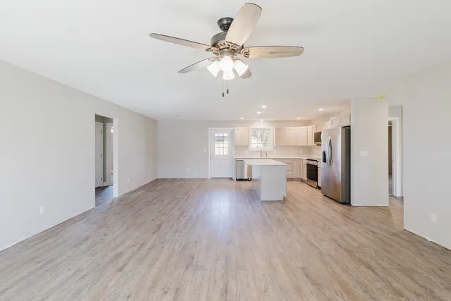 a view of an empty room with wooden floor and a ceiling fan