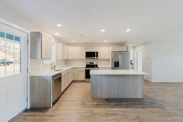 a large kitchen with stainless steel appliances a sink a stove a refrigerator cabinets and a window