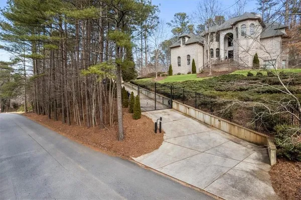 a view of a white house next to a road with large trees