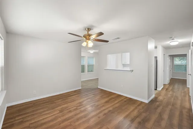 a view of an empty room with wooden floor and a ceiling fan