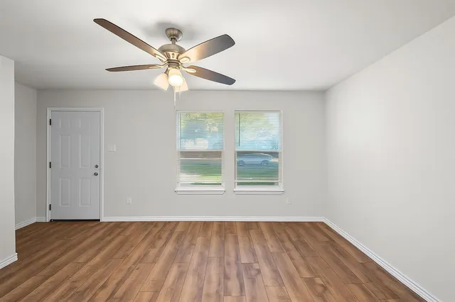 an empty room with wooden floor fan and windows