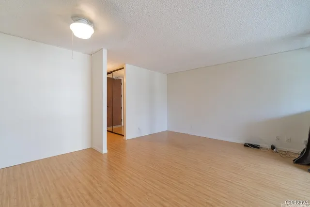 a view of an empty room with wooden floor and fan