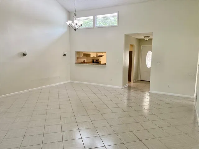 an empty room with kitchen view and a chandelier fan