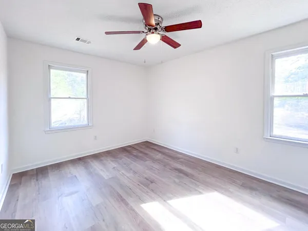 an empty room with wooden floor ceiling fan and windows