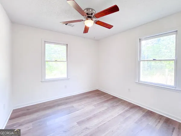 an empty room with wooden floor ceiling fan and windows