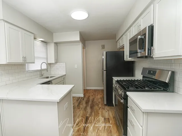 a kitchen with stainless steel appliances a sink a stove a microwave a refrigerator a cabinets and wooden floor