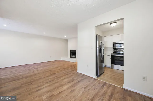 an empty room with wooden floor and kitchen view