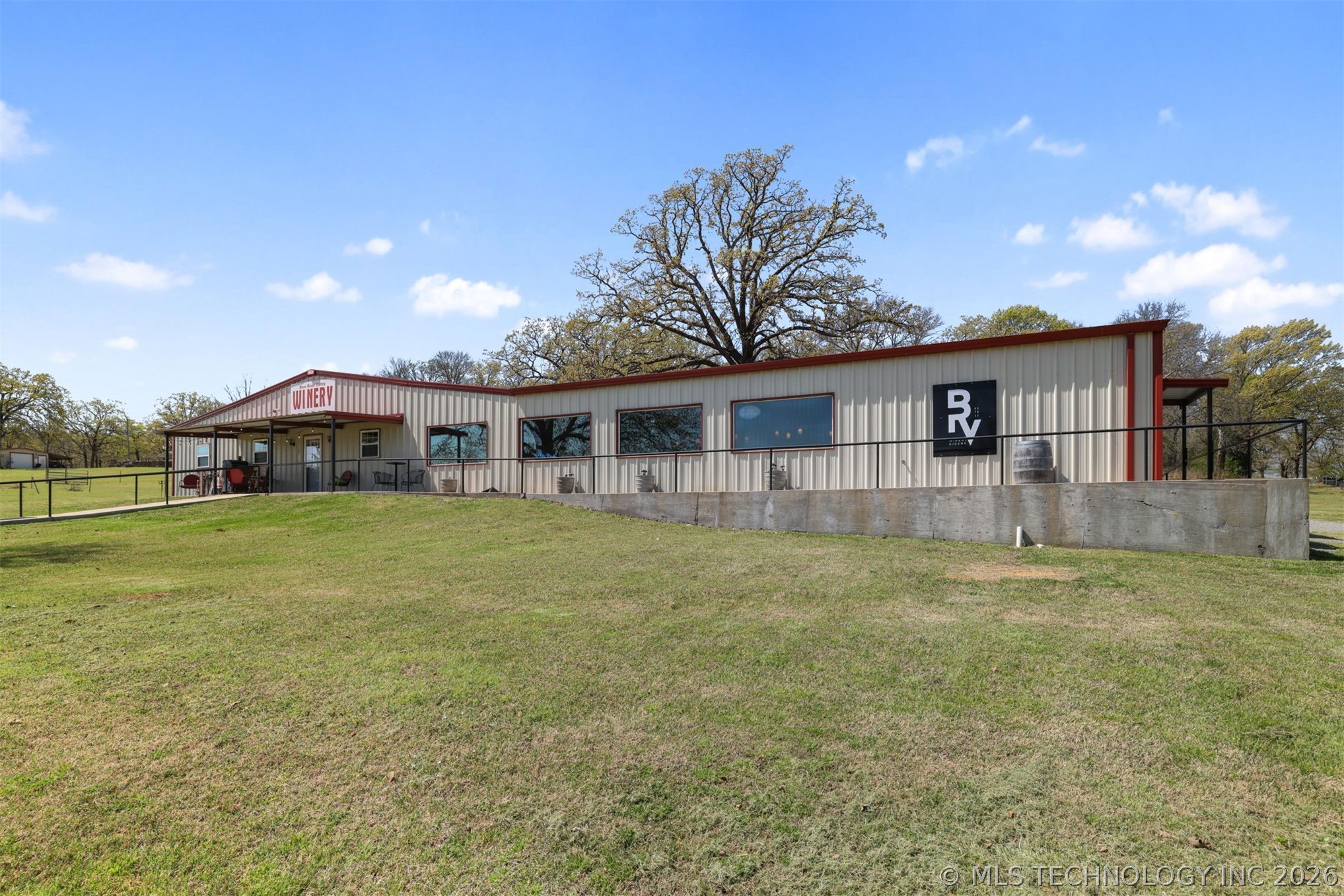 3565 Sawmill Road Caddo, OK 74729 - Photo 2 of 32 Corrugated metal siding structure featuring a red-trimmed roof, covered front entry, multiple large windows, and a concrete foundation