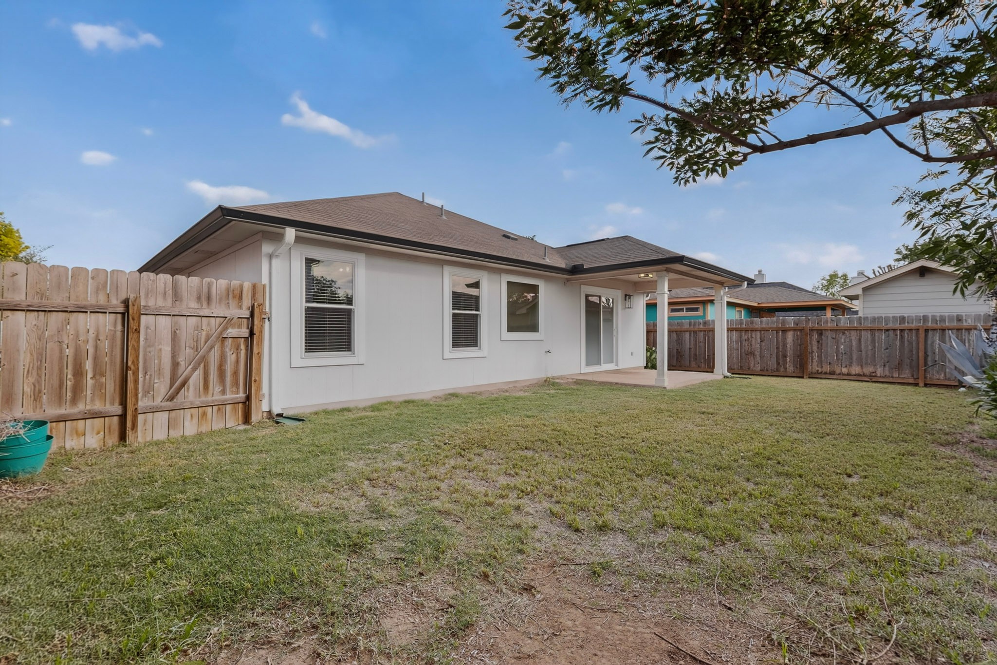 3906 Reeders Drive Austin, TX 78725 - Photo 35 of 36 Expansive backyard featuring a covered patio, white stucco exterior, brown shingle roof, wood privacy fencing, and multiple windows