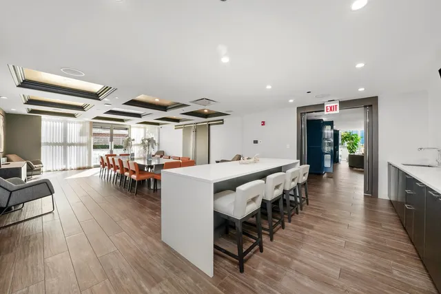 a dining hall with stainless steel appliances a dining table chairs and couches with wooden floor