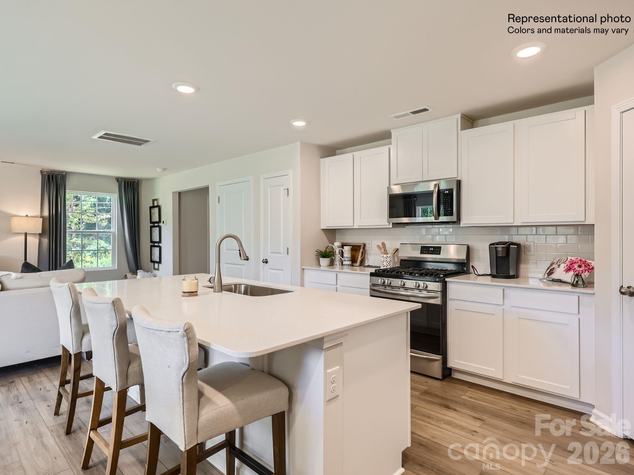 a kitchen with stainless steel appliances granite countertop a stove a sink a microwave a refrigerator with white cabinets and wooden floor